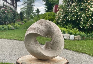Skulptur „Alles im Fluss II“ von Sabine Classen – organische, kreisförmige Keramikform mit strukturierter Oberfläche, ausgestellt auf einem Baumstamm-Sockel im Garten des Schwandorfer Hofs in Salem am Bodensee, Keramikskulptur Verkaufsobjekt